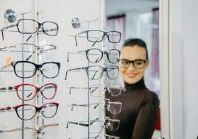 Stand mit Brille im das Geschäft von Optik. schön Mädchen im Brille auf ein Hintergrund. selektiv Fokus foto