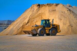 Instandhaltung von Gelb Bagger auf ein Konstruktion Seite? ˅ gegen Blau Himmel. Rad Lader im Sandhaufen Hintergrund. selektiv Fokus. foto