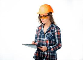 attraktiv Frau Baumeister im Orange Helm und schützend Brille mit Mappe im Hand Schreiben auf Weiß Hintergrund. ziemlich Ingenieur im Hemd Schreiben mit Kugelschreiber Stift auf schwarz Mappe foto