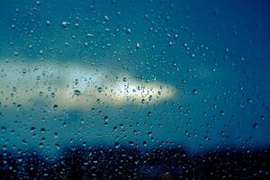 Wasser Tropfen auf Glas gegen Blau wolkig Himmel im das Abend. Tropfen von Regen auf Fenster im das dunkel Hintergrund. Nahansicht. foto