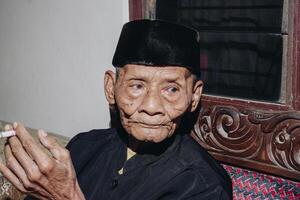 Porträt von ein Alten asiatisch Mann Rauchen ein Zigarette. foto