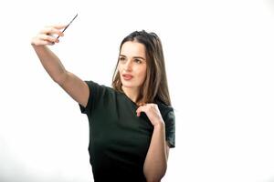 Frau macht ein Selfie im ein Studio mit ein Smartphone. Brünette mit ein Hand in der Nähe von kinn. foto