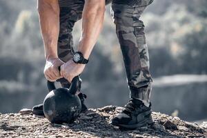 stark männlich Waffen auf das Kettlebell von 24 Kilo. muskulös Hände mit ein Uhr auf das Gewicht. Bodybuilder Hände und Beine schließen oben auf das Felsen. foto