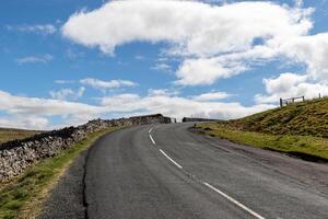 leeren Land Straße mit Stein Wände unter ein Blau Himmel mit Wolken im Yorkshire Täler. foto
