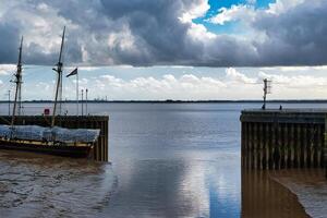 heiter Hafen Szene mit festgemacht Segelboot, Ruhe Wasser, und wolkig Himmel, reflektieren ein still maritim Landschaft. foto