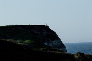 Silhouette von ein Person Stehen auf ein Cliff mit Blick auf das Meer mit klar Himmel im Flamborough, England. foto