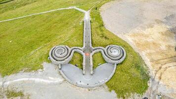 Antenne Aussicht von ein einzigartig Spiral- Skulptur auf ein grasig Landschaft mit ein Weg führen zu Es. foto