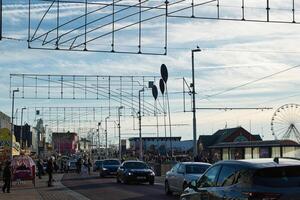 geschäftig Straße Szene mit Fußgänger und Autos, Fahrgassen Overhead, und ein Ferris Rad im das Entfernung unter ein klar Himmel im blackpool, England. foto