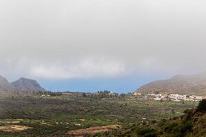 neblig Landschaft mit Berge und ein Küsten Dorf unter ein wolkig Himmel Berg Landschaft mit Blau Himmel und Wolken im Teneriffa. foto