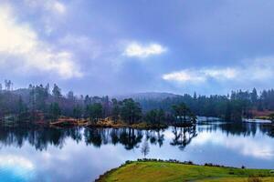 heiter See mit Reflexionen von Bäume unter ein wolkig Himmel beim Dämmerung. foto