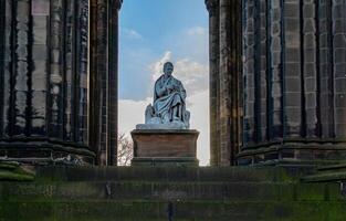 Statue von ein historisch Zahl gerahmt durch Stein Säulen unter ein klar Blau Himmel im Edinburgh, Schottland. foto