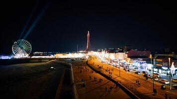 Nacht Aussicht von ein lebhaft Promenade mit beleuchtet Ferris Rad und Turm, geschäftig mit Aktivität und Beleuchtung im Rückstau, England. foto