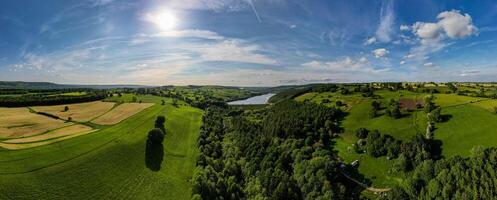 Panorama- Aussicht von ein üppig Grün Senke mit ein Fluss, unter ein riesig Blau Himmel mit verstreut Wolken. foto