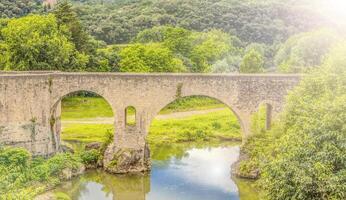 alt Stein Brücke im das Grün Wald über das Fluss foto