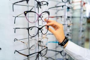 Reihe von Brille beim ein Optiker. Brille Geschäft. Stand mit Brille im das Geschäft von Optik. Frau Hand wählen Brille. präsentieren Brille. foto