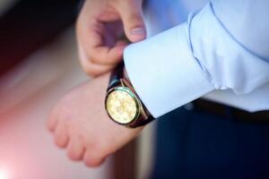 Geschäftsmann Überprüfung Zeit auf seine Handgelenk betrachten, Mann Putten Uhr auf Hand. Bräutigam bekommen bereit im das Morgen Vor Hochzeit Zeremonie foto