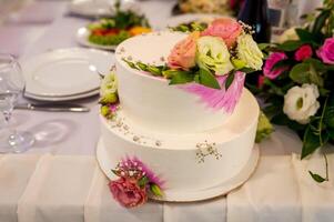 Weiß Hochzeit Kuchen auf ein Tabelle mit Blumen auf das Hintergrund. Rosen auf ein Kuchen. foto