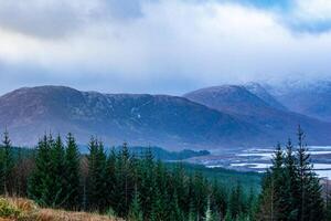 neblig Berg Landschaft mit Wald im das Vordergrund und wolkig Himmel über im Schottland. foto