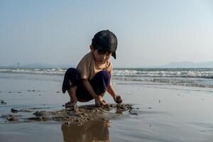 wenig asiatisch Junge spielen im das Sand beim das Meer Strand foto