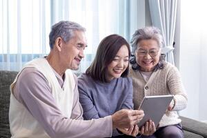 asiatisch Familie Wiedervereinigung von Senior Vater, Mutter und Tochter Sitzung auf Couch mit glücklich Lächeln im Pensionierung Zuhause während suchen beim alt nostalgisch Foto im das Vergangenheit