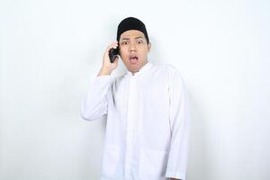 asiatisch Muslim Mann sieht aus schockiert während reden auf das Telefon foto