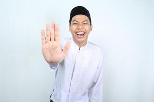 asiatisch Muslim Mann Lachen und erreichen Palme beim Kamera sagen halt Geste isoliert auf Weiß Hintergrund foto