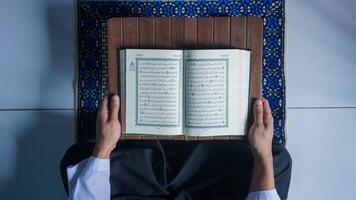 oben Aussicht von ein Muslim Mann lesen das Koran auf ein Gebet Matte foto