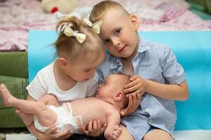 wenig Bruder und Schwester jubeln beim das Neugeborene Baby. drei Kinder von anders Alter im ein Zuhause Umfeld. das groß Familie. foto