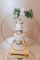 ein dreistufig Hochzeit Kuchen dekoriert mit Blumen steht auf ein gespiegelt Tisch. dekorativ Hochzeit Kuchen. Schönheit ist im das Einzelheiten. foto