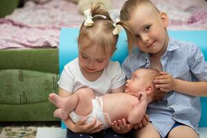 wenig Bruder und Schwester jubeln beim das Neugeborene Baby. drei Kinder von anders Alter im ein Zuhause Umfeld. das groß Familie. foto