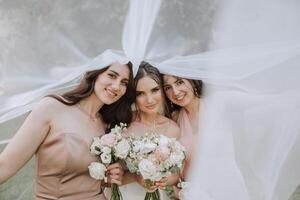 Brautjungfern sind eingewickelt im ein Schleier. das Braut ist halten ein Strauß. lange Schleier. Hochzeit im Natur. lächelnd Mädchen im identisch Kleider. foto