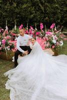 schön Paar Sitzung und umarmen draußen auf ihr Hochzeit Tag, entspannend auf das Beste Sommer- Tag. ein gut aussehend Bräutigam und ein elegant Braut im ein großartig Hochzeit Kleid. foto