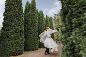 das Bräutigam angehoben das Braut im seine Waffen und ist kreisen im ein schön Garten. Braut und Bräutigam Tanzen im das Hinterhof. foto