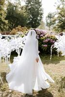 ein schön Brünette Braut im ein elegant Kleid ist Gehen im ein Park mit Grün Gras und Rosa Hortensie Blumen. Morgen, Sitzungen, Hochzeit Porträt von ein süß Mädchen. Fotografie und Konzept. Sommer. foto