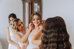 Hochzeit Morgen. Brautjungfern Hilfe stellen auf das Weiß Hochzeit Kleid. ein jung Frau ist vorbereiten zu Treffen ihr Bräutigam und haben Spaß mit ihr freunde foto