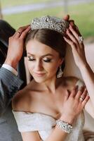 Porträt von ein Braut mit ein Krone auf ihr Kopf. das Bräutigam unterstützt das Braut Krone. das Konzept von ein königlich Hochzeit. Vertikale Foto. foto