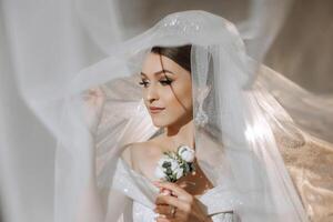 schön jung Braut halten Schleier im Weiß Hochzeit Kleid, Porträt von Brünette Braut im Hotel Zimmer, Morgen Vor Hochzeit. foto