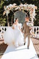 das Braut und Bräutigam sind Gehen gegen das Hintergrund von das Hochzeit Bogen. draussen Hochzeit Zeremonie. Bräutigam und Braut auf das Hintergrund von das Hochzeit Bogen. foto