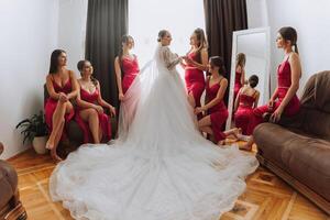 Hochzeit Morgen. Brautjungfern Hilfe stellen auf das Weiß Hochzeit Kleid. ein jung Frau ist vorbereiten zu Treffen ihr Bräutigam und haben Spaß mit ihr freunde foto