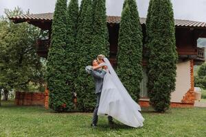das Bräutigam angehoben das Braut im seine Waffen und ist kreisen im ein schön Garten. Braut und Bräutigam Tanzen im das Hinterhof. foto