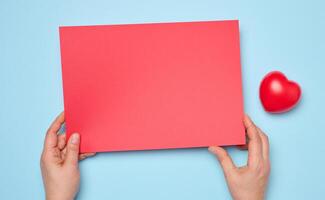 weiblich Hände halten ein leer rot Blatt von Papier auf ein Blau Hintergrund foto