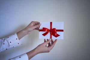 Geschenk Zertifikat im rot und Weiß Farben im weiblich Hände auf ein Weiß Mauer Hintergrund foto