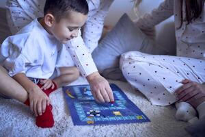 Mutter mit Teenager Tochter und wenig Sohn im Pyjama spielen Tafel Spiele auf das Fußboden foto