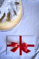 ein Geschenk Zertifikat im rot und Weiß Farben auf das Tabelle Nächster zu ein Kuchen bestreut mit pulverisiert Zucker foto