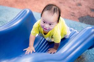 Porträt von asiatisch Baby Junge glücklich spielen auf das Spielplatz, und gleiten Nieder ein Blau gleiten. süß Kind klettert das rutschen auf das Spielplatz. Kleinkind Kind alt ein Jahr alt. echt Personen. foto