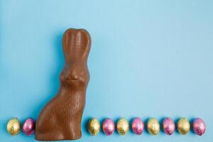 Milch Schokolade Hase und Reihe von Ostern Süßigkeiten Eier eingewickelt im Rosa und golden vereiteln auf Blau Hintergrund foto