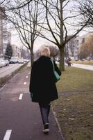 Porträt von ein stilvoll alt Frau im ein schwarz Mantel mit Grün Zubehör auf ein Frühling Straße foto