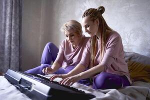 ein 60 Jahre alt Mutter und ein 40 Jahre alt Tochter abspielen das Tastatur zusammen auf das Bett beim Zuhause foto