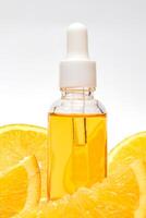 ein Nahansicht von ein Vitamin c Serum Flasche mit ein Tröpfchen, umgeben durch frisch, beschwingt Orange Scheiben. Attrappe, Lehrmodell, Simulation foto