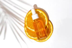 Gesichts- Öl Tropfer Flasche mit Vitamin c auf geschnitten Orange mit Palme Blatt Schatten. Haut Pflege Konzept foto